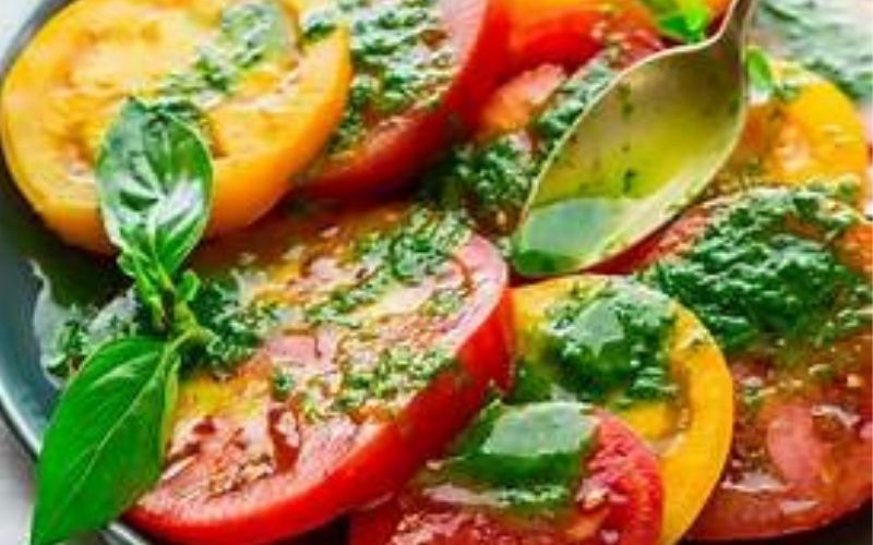 Sliced tomatoes are drizzled with pesto